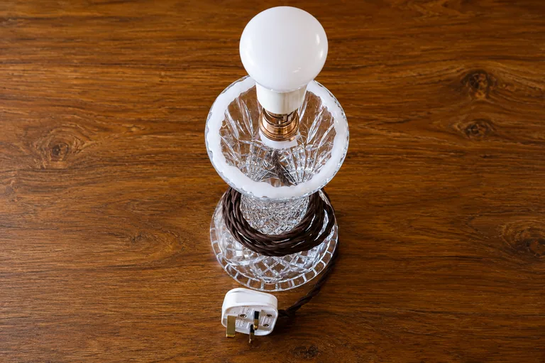 A crystal vase lamp prototype with a bulb, copper-toned fitting, and fabric cable on a wooden table