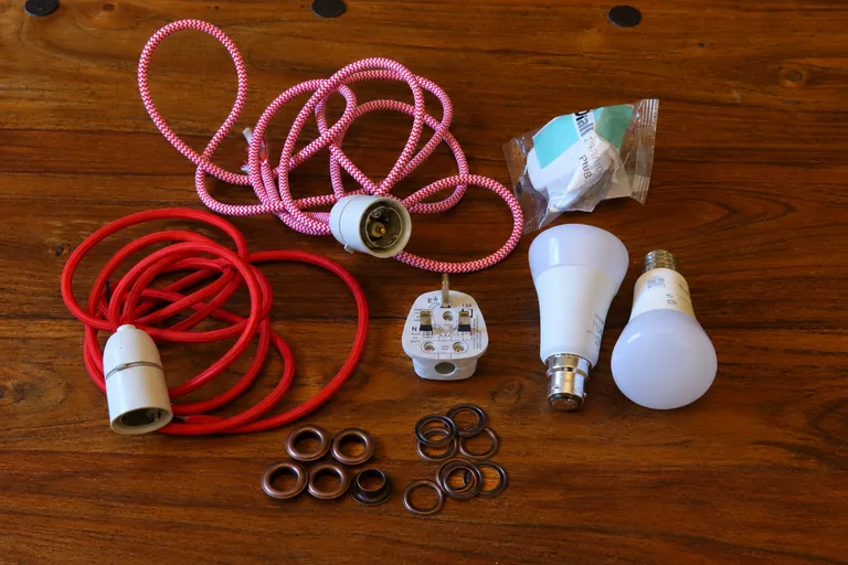 Lamp-making components laid out on a wooden table, including red cable, bulb fittings, plugs, and bulbs